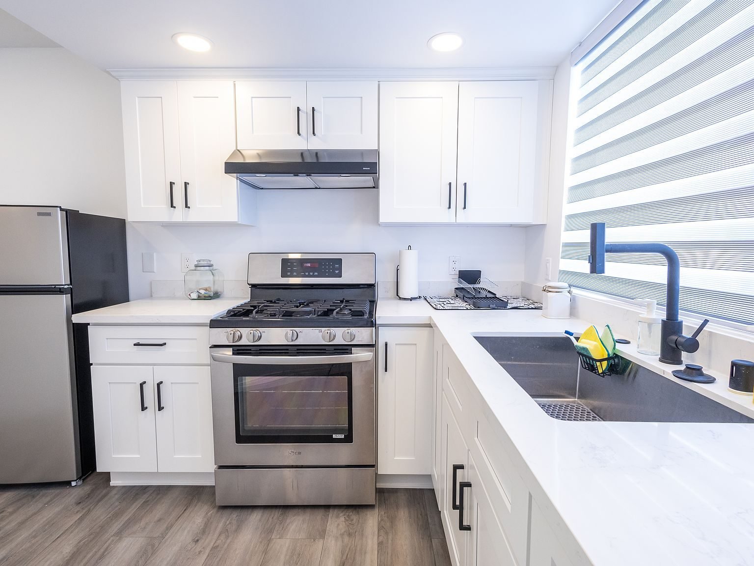 White kitchen with quartz countertops, gas range, and stainless refrigerator