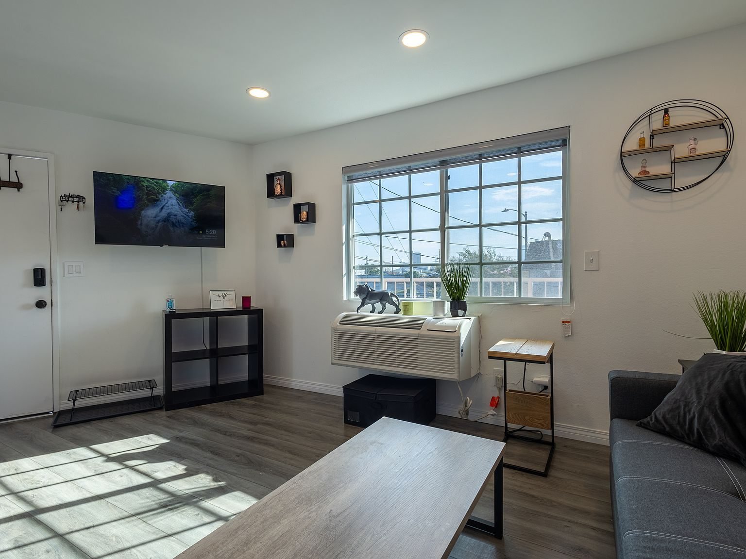 Bright living room in Apartment A with a large window, sofa, and wall-mounted TV